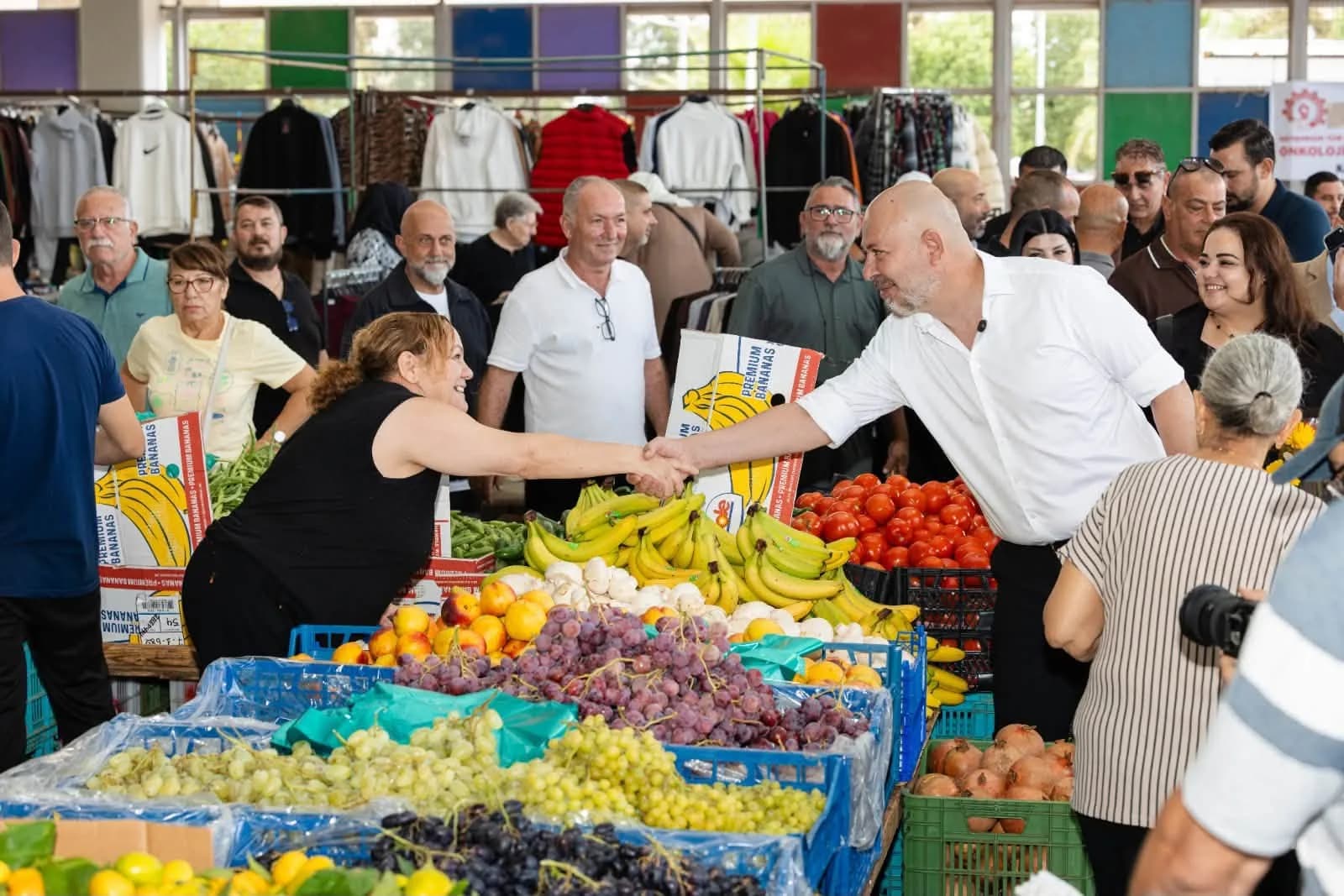 Koral Bozkurt, pazar alanında meyve tezgâhındaki bir esnafla tokalaşırken